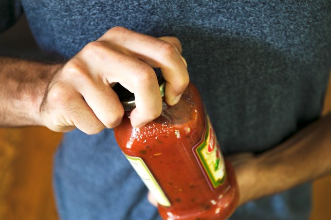 man tightly gripping a jar of sauce to open it
