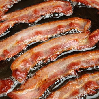 Bacon strips or rashers being cooked in frying pan.; Shutterstock ID 153808931