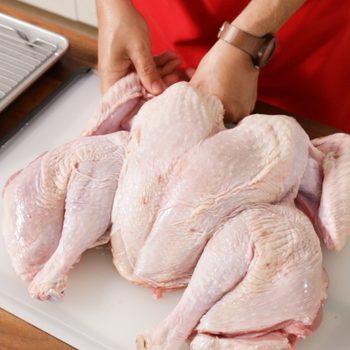 How to Spatchcock a Turkey with a raw turkey on a cutting board in the kitchne
