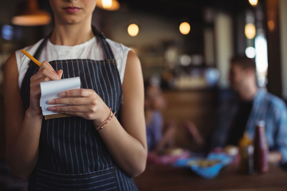 Mid section of waitress taking order at restaurant