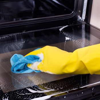 Close up of female hand with yellow protective gloves cleaning oven door