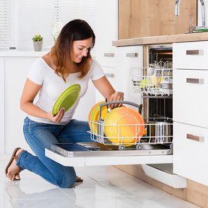 Happy Young Woman Arranging Plates In Dishwasher At Home