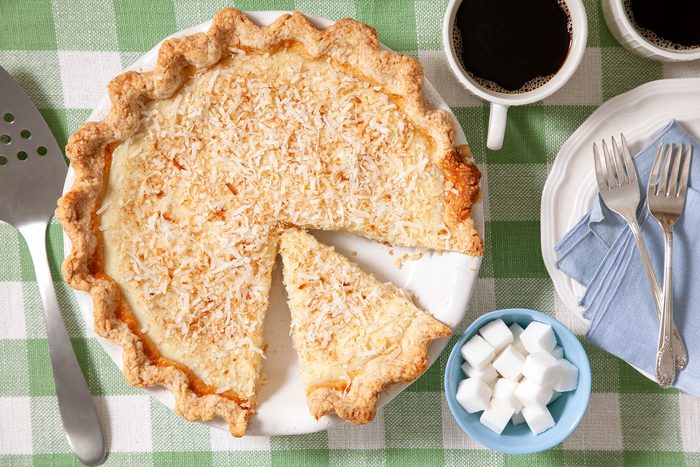 Coconut Custard Pie in Ceramic Plate with Coffee in Cups and Sugar Cubes in Small Bowl with Forks on Plate