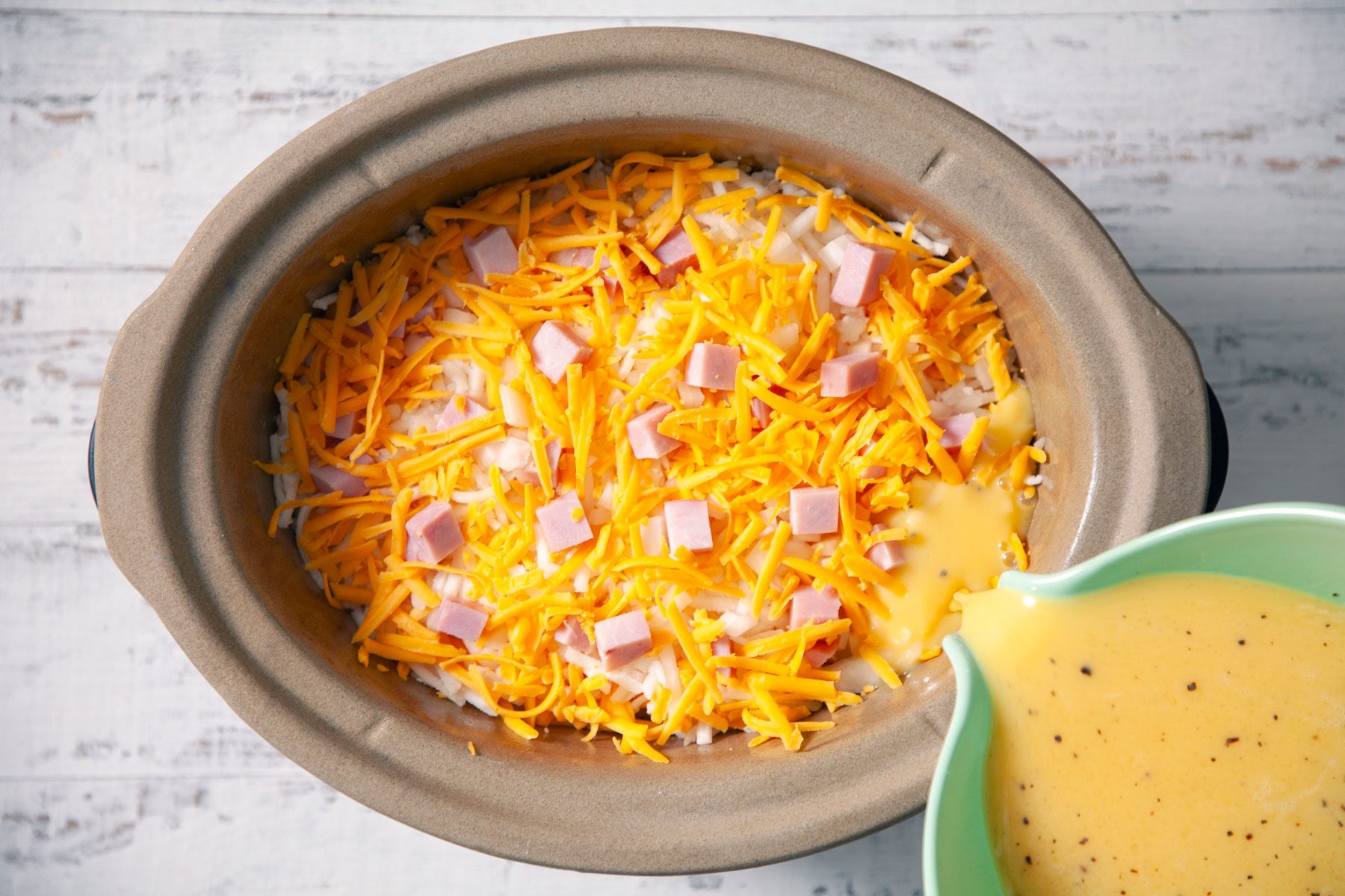 Eggs and milk mixture being poured on Ham and cheese