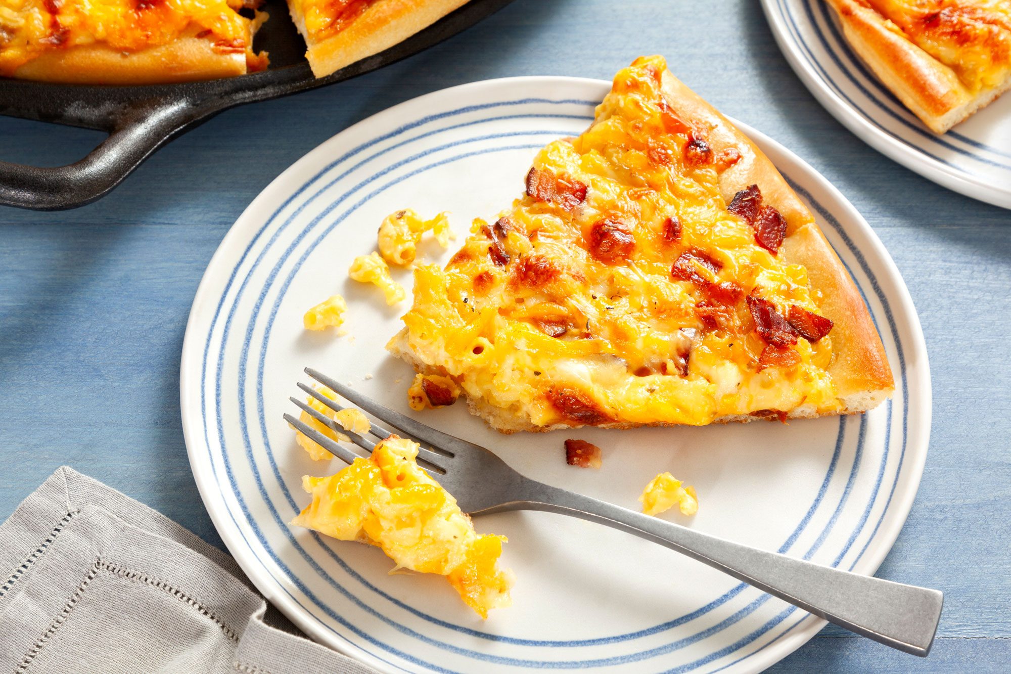 Mac And Cheese Pizza Slice on a White Ceramic Plate with Fork on Textured Blue Background
