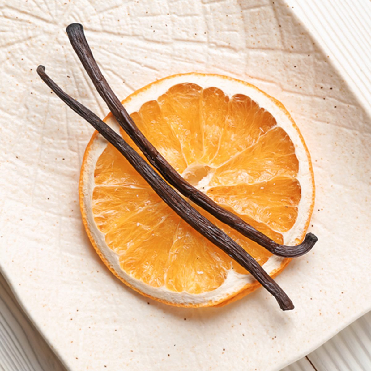 Plate with dry orange slice and aromatic vanilla sticks on white wooden background; Shutterstock ID 1283600635; Job (TFH, TOH, RD, BNB, CWM, CM): TOH