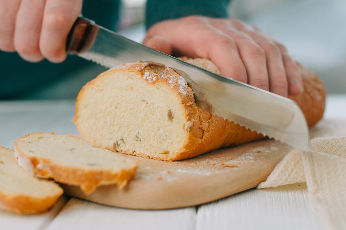 Male hands cutting wheaten bread on the wooden board