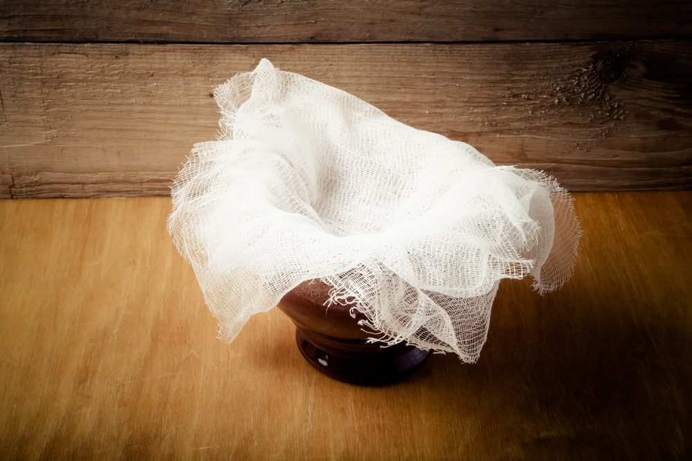Clay pot with ghee under cheesecloth on light wooden table.