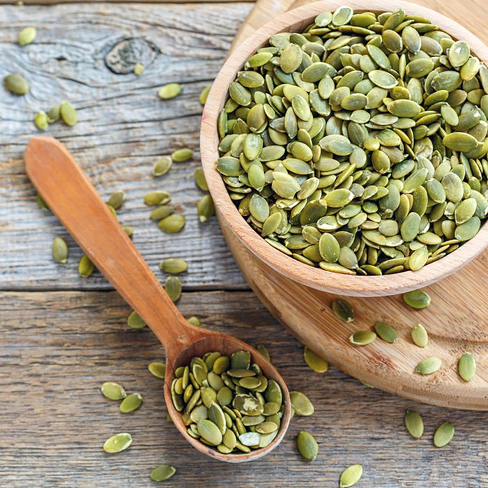 Bowl with pumpkin seeds and a wooden spoon on a wooden table.
