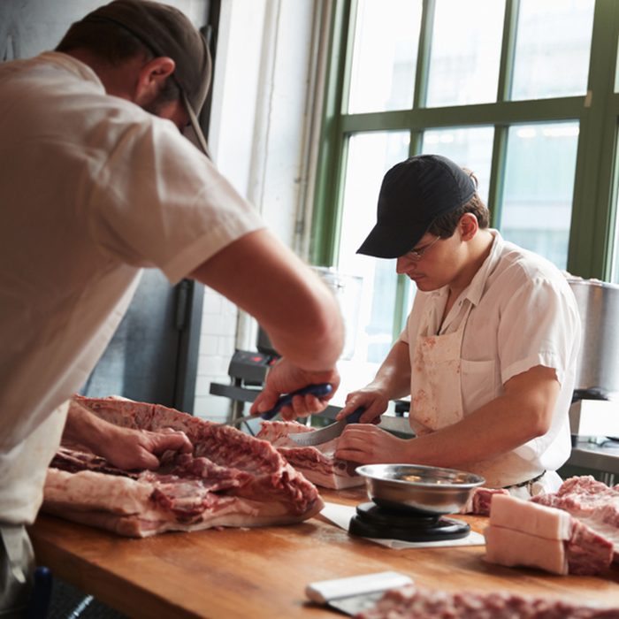 Two butchers cutting meat to sell at a butcher's shop