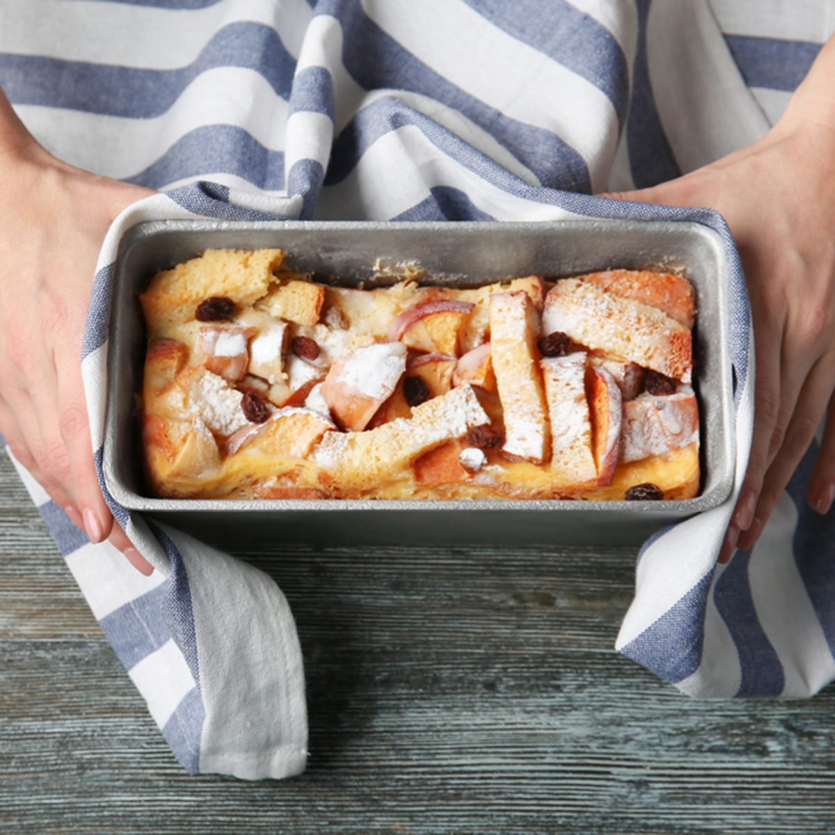 Female hands holding casserole dish with baked bread pudding on wooden table