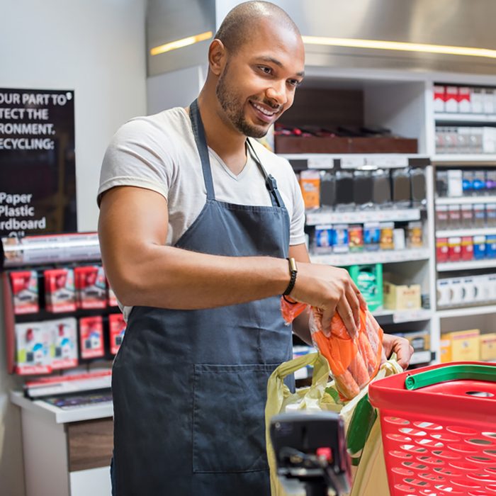 Smiling salesman putting vegetables in bag for customer after billing