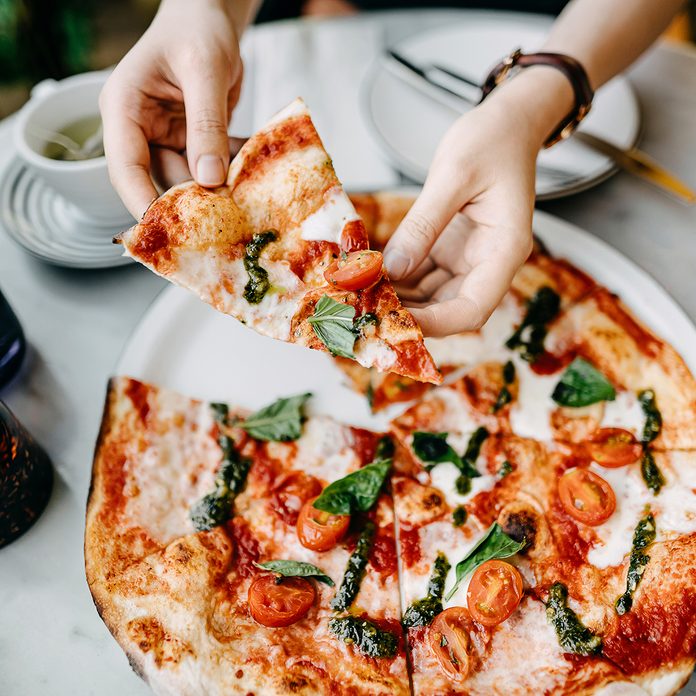 Overhead View Of Woman's Hand Getting A Slice Of Freshly Made Pizza And Enjoying Her Meal In An Italian Restaurant