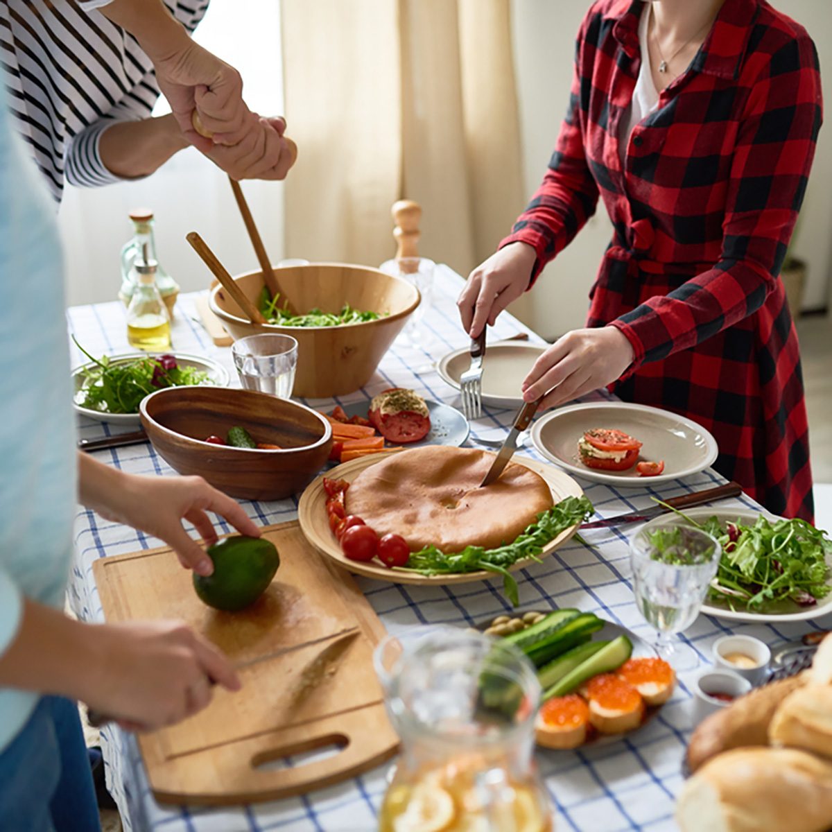 Low section of unrecognizable people cutting pie and vegetables standing around dinner table with homemade food on it