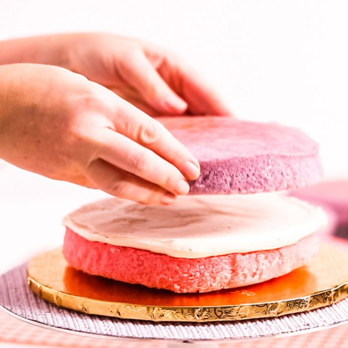 Baker assembling pink and purple cake layer to make unicorn cake for little girl's birthday party.