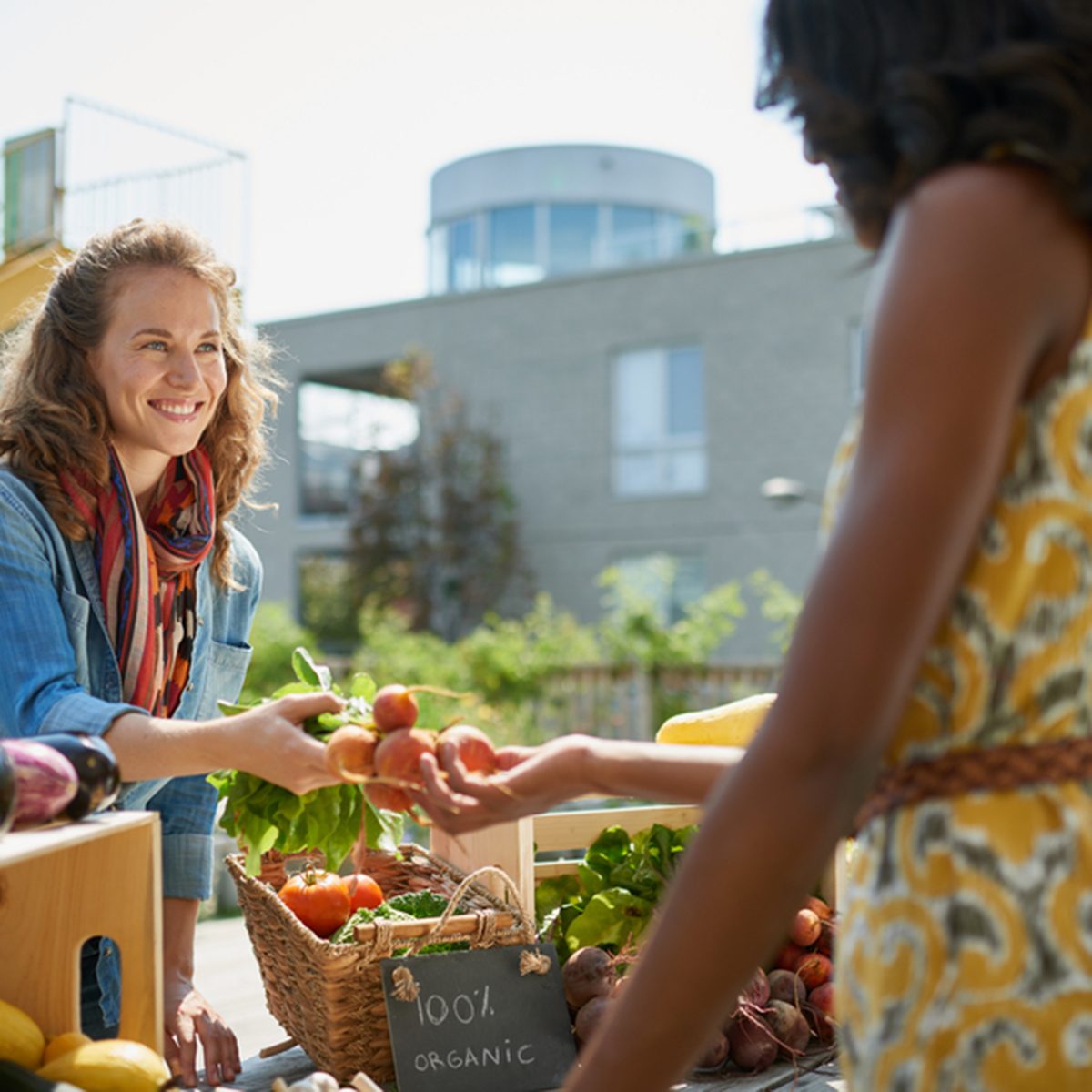 Friendly woman tending an organic vegetable stall at a farmer's market and selling fresh vegetables from the rooftop garden