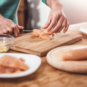 Woman cutting chicken breast on the table