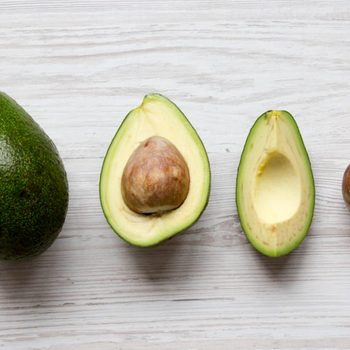 Whole and chopped avocados on white wooden background, overhead view. Top view, from above, flat lay.