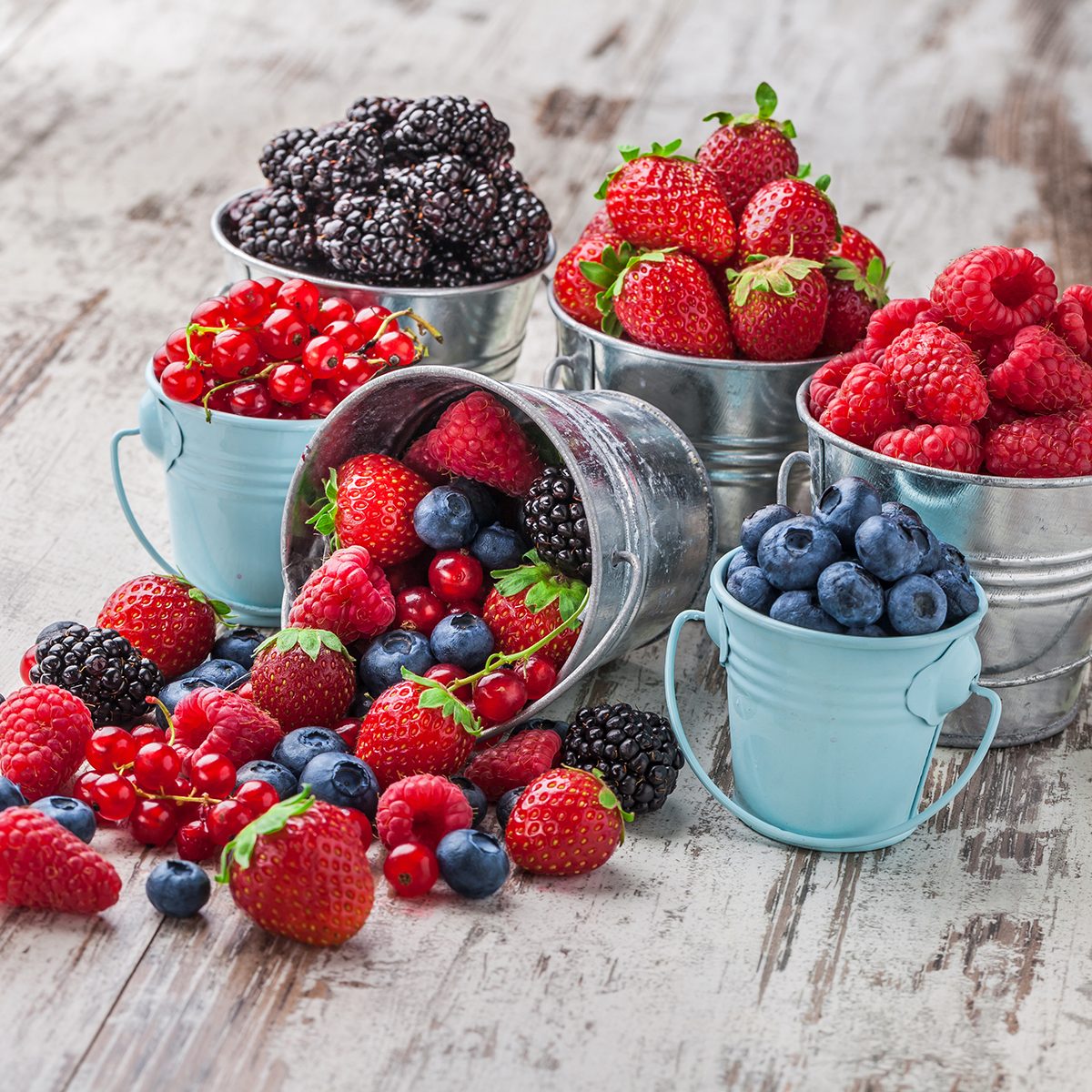 Berries mix blueberry, raspberry, red currant, strawberry, in five old tin cans spilled on white rustic wooden table in studio