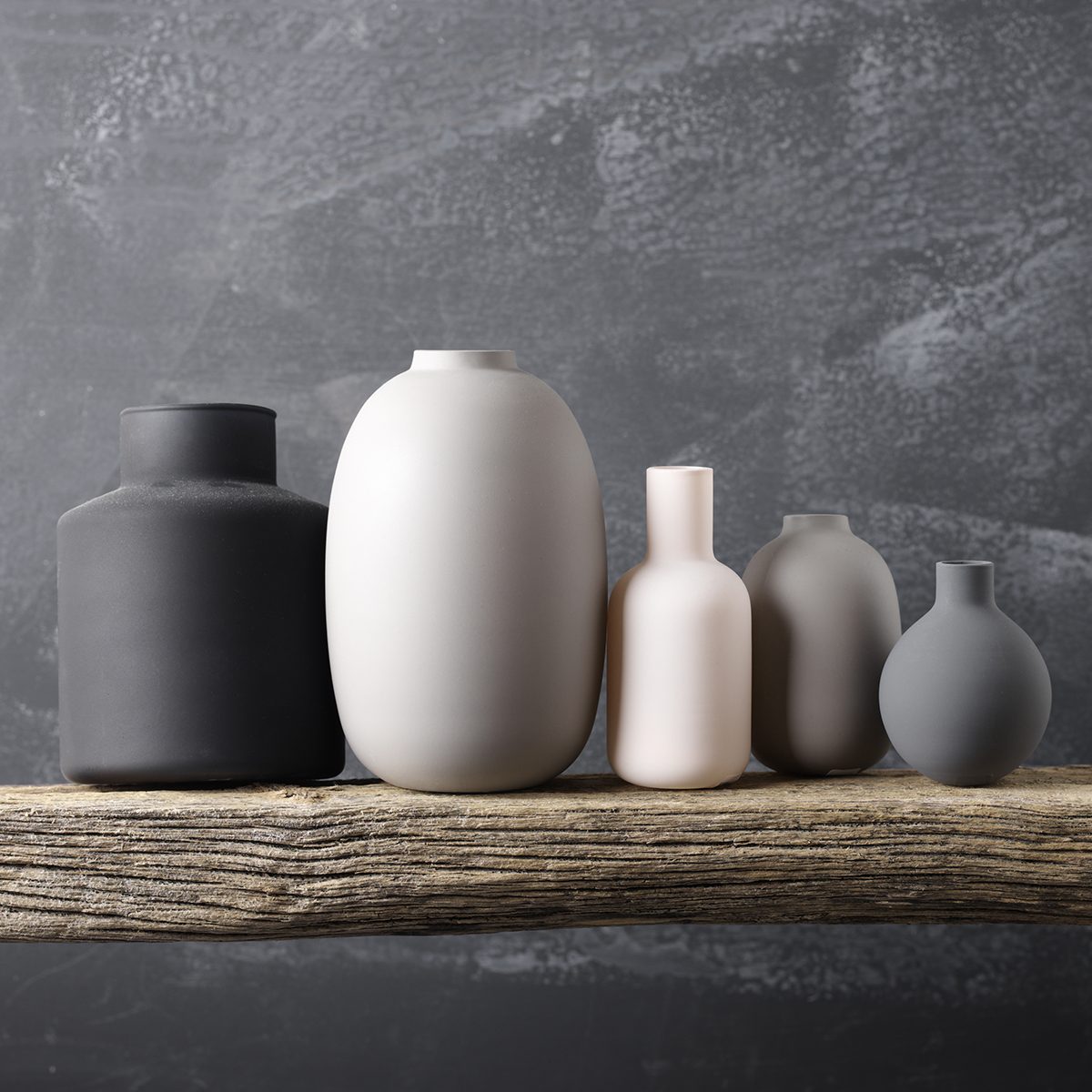 Home decor - various neutral colored vases on rough distressed wooden shelf against grey wall.