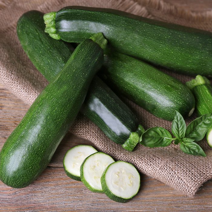 Fresh zucchini with basil on wooden table close up
