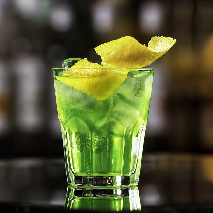 Glass of cocktail green fairy with lemon and absinthe at bar stand festive background.