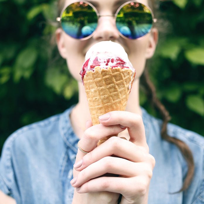 Outdoor closeup fashion portrait of young hipster crazy girl eating ice cream in summer hot weather in round mirror sunglasses have fun and good mood.