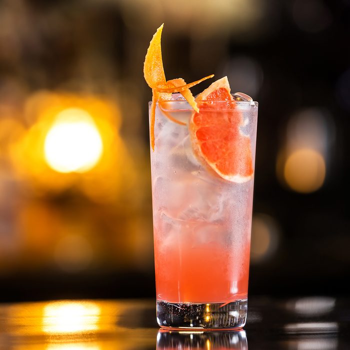 Closeup glass of greyhound cocktail decorated with grapefruit at bright bar counter background.