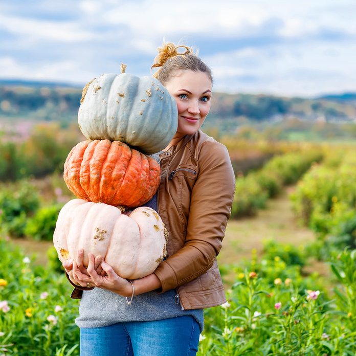Beautiful young woman with three huge different pumpkins on a farm or patch.