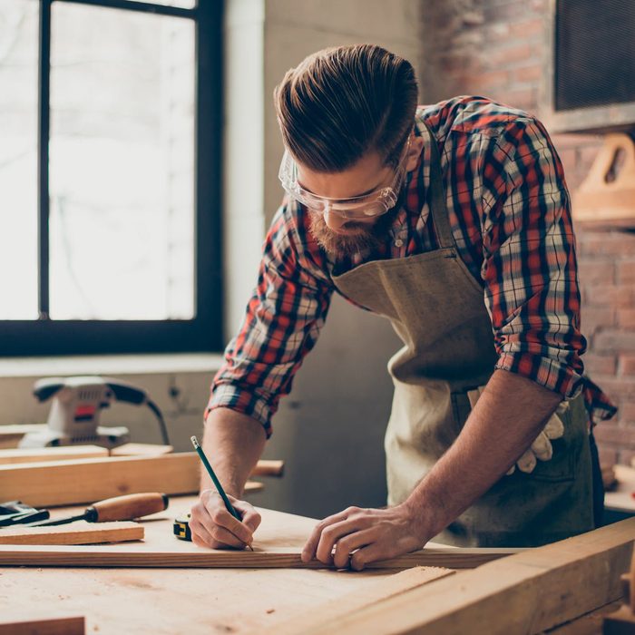 Man draws a measuring mark with a pencil on a piece of wood.