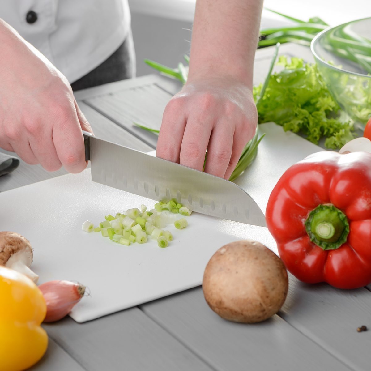 Chef cook chopping spring onions on a white board.