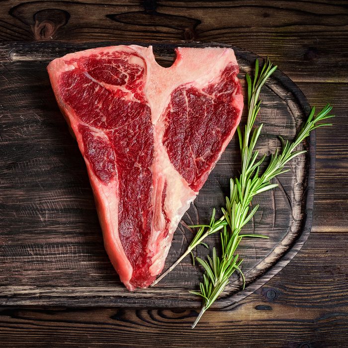 raw porterhouse steak, dry-aged on wooden Board with herbs