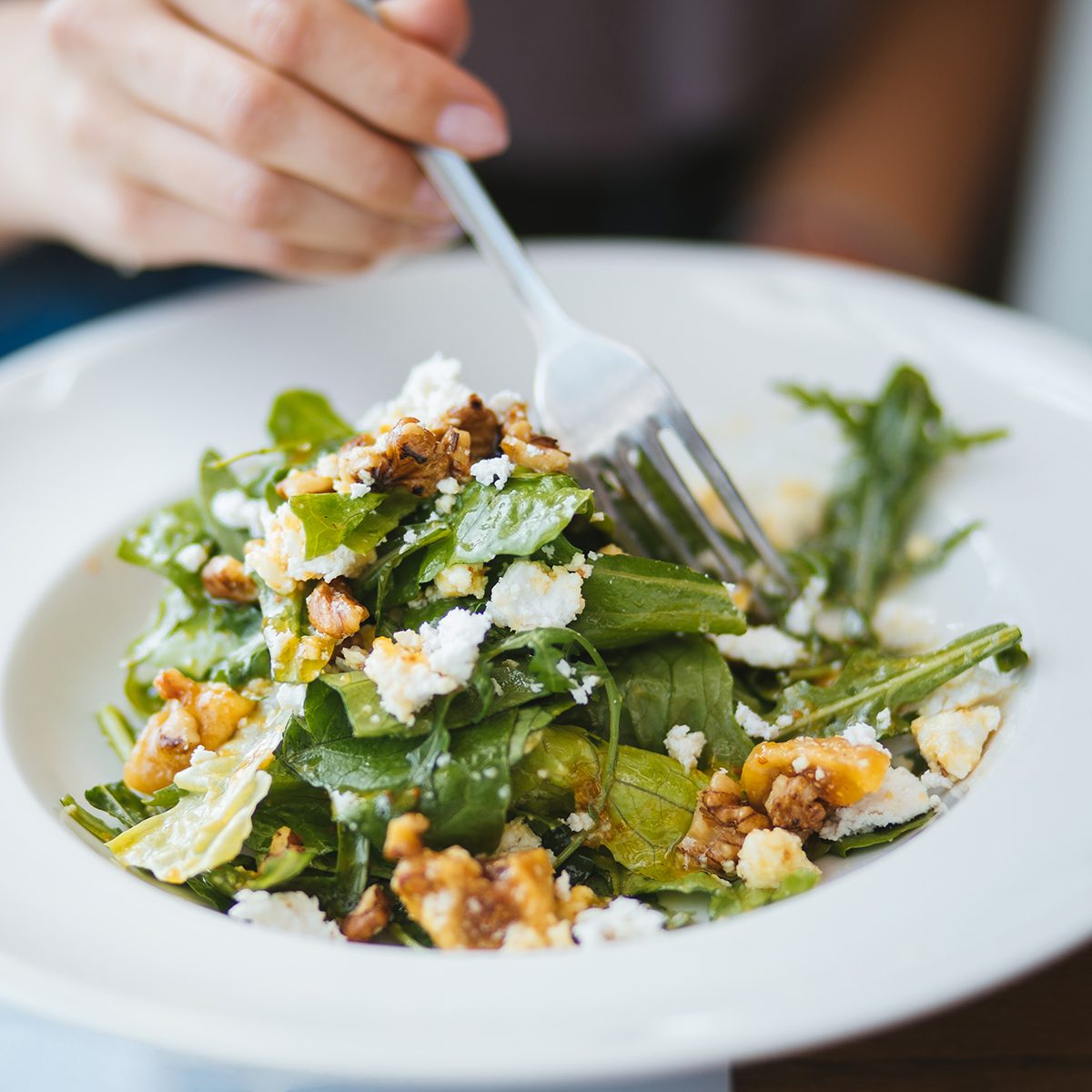 Close up of woman's hand eating a Mediterranean vegetarian salad for dinner