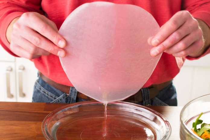 A person dipping rice paper into water to make homemade spring rolls.