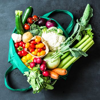 Colorful organic vegetables in green eco shopping bag - captured from above (top view, flat lay). Black chalkboard (blackboard) as background. Layout with free text (copy) space.