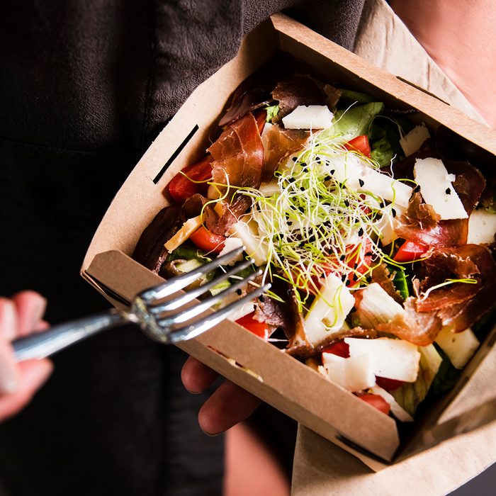 Woman's hand is holding a take away fresh salad in a lunch box. Gourmet conception.