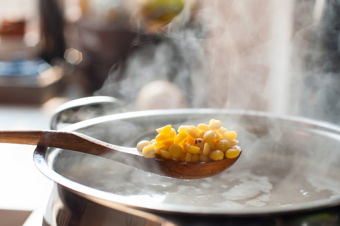 Saucepan and wooden spoon with split pea. Boiling broth with steam. Making soup.