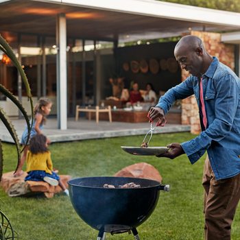 man grilling in his backyard with family