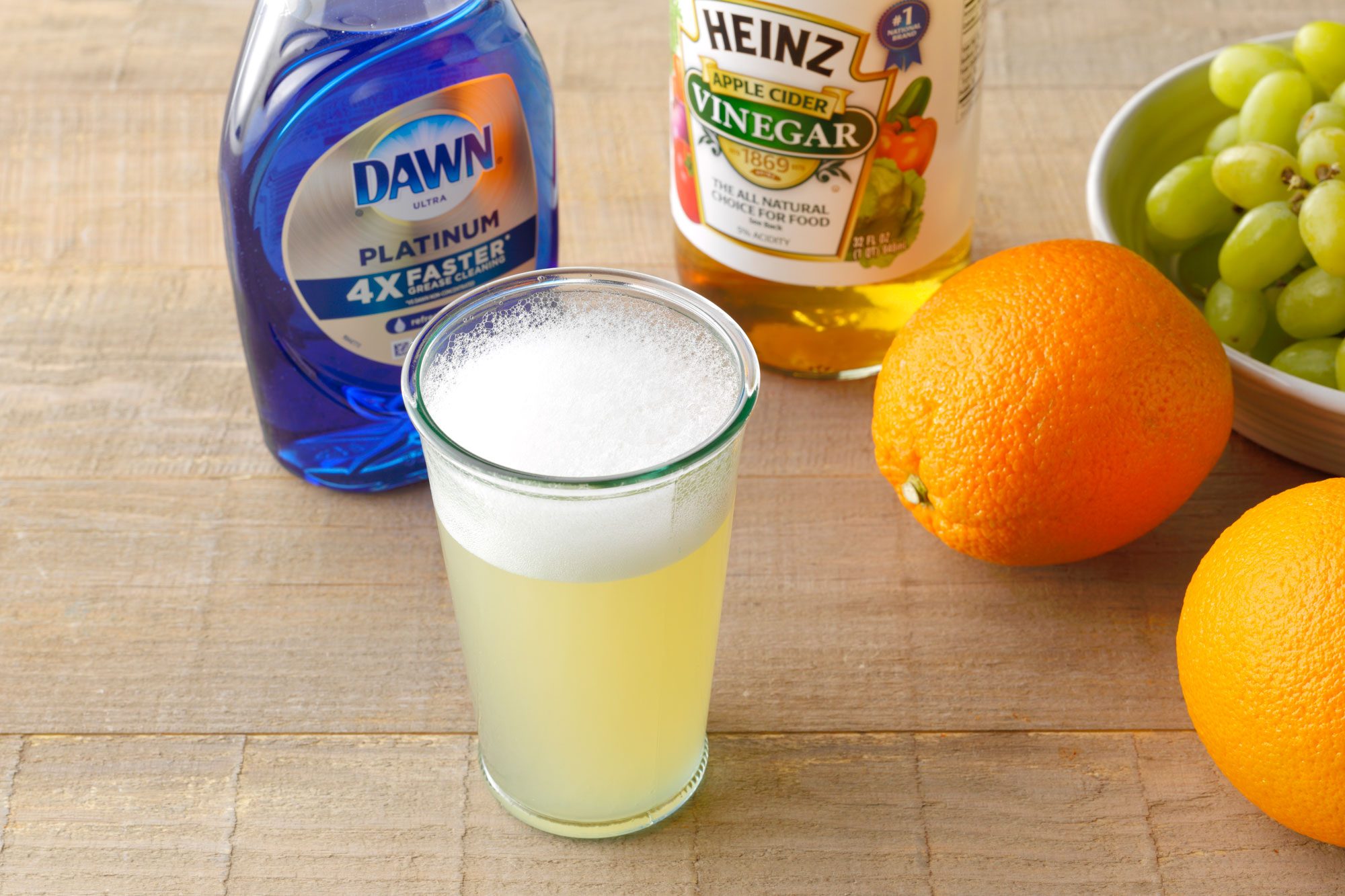 sudsy trap 4 mixture in a glass with dawn dish soap, apple cider vinegar bottle, and fresh fruit nearby on a wooden surface.