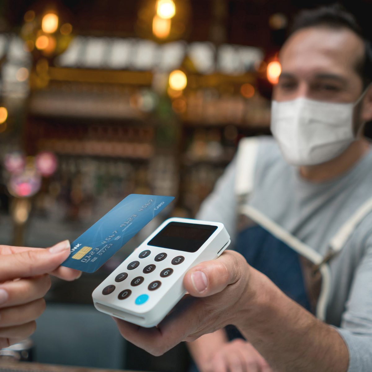 Waiter wearing a facemask while getting a contactless payment at a restaurant