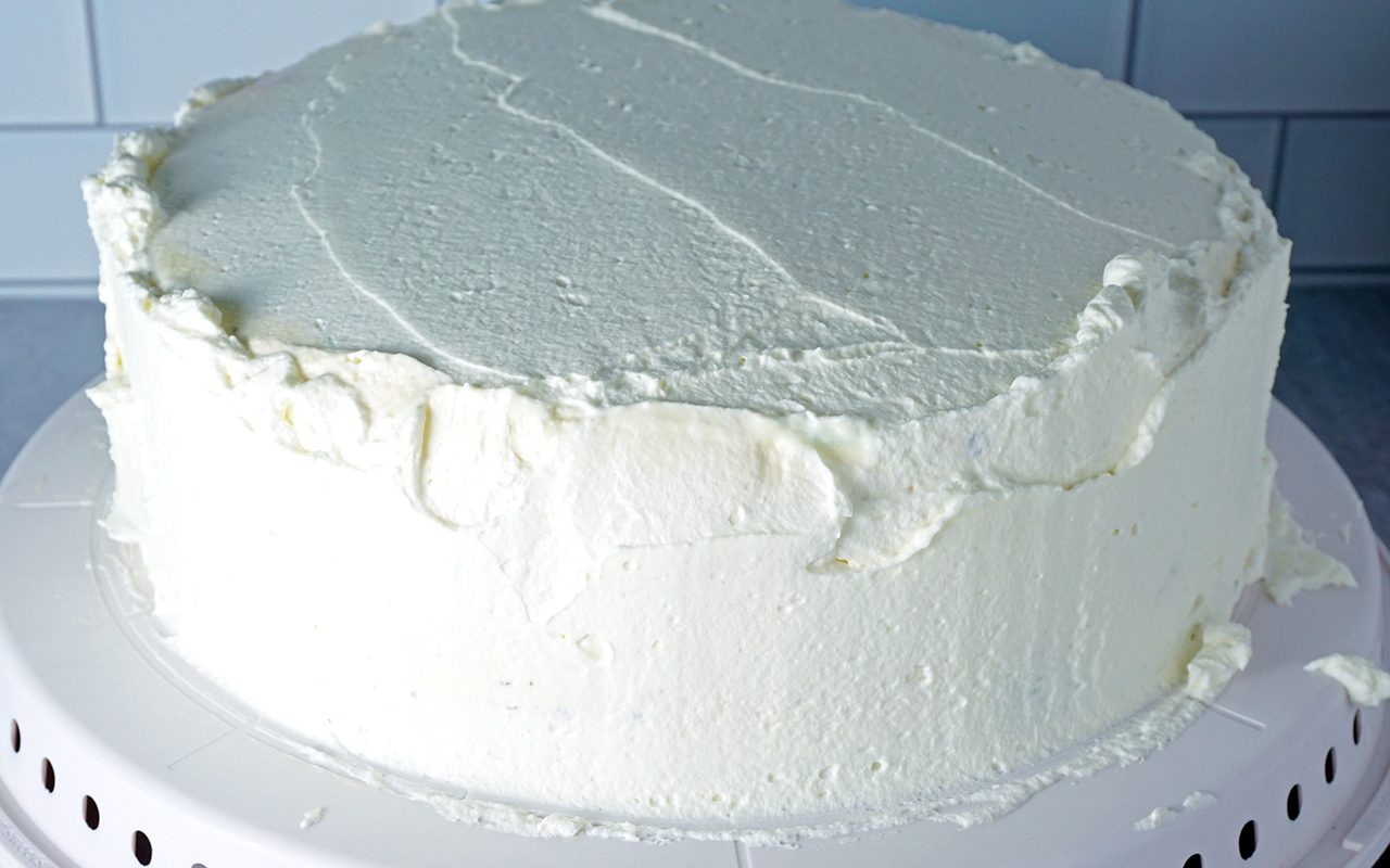 spreading a thin layer of whipped cream frosting onto ice cream cake