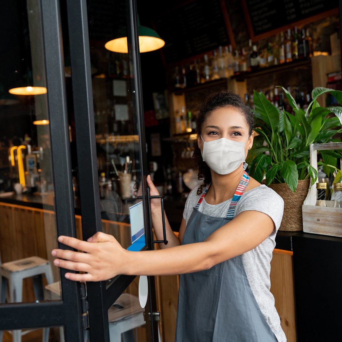 Happy business owner opening the door at a cafe wearing a facemask