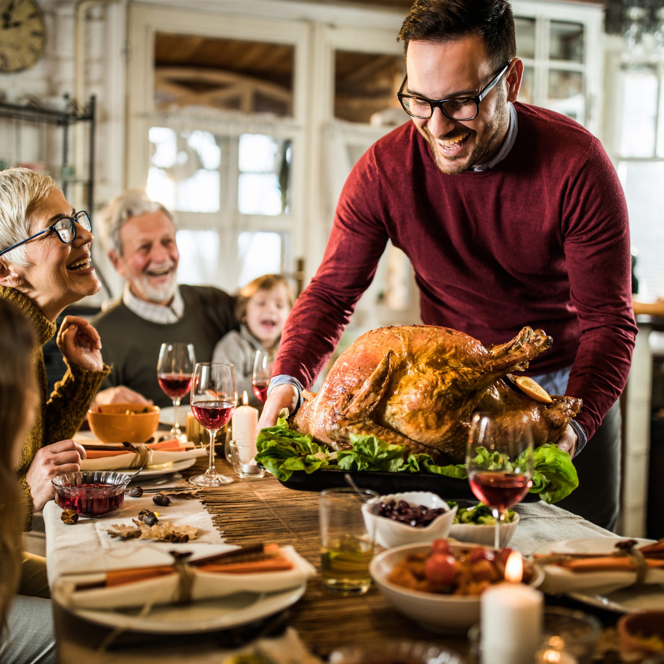Happy man serving roasted turkey to his family during Thanksgiving dinner at dining table.