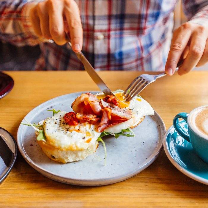 Man eating breakfast with egg, bacon, arugula on brioche bun and coffee