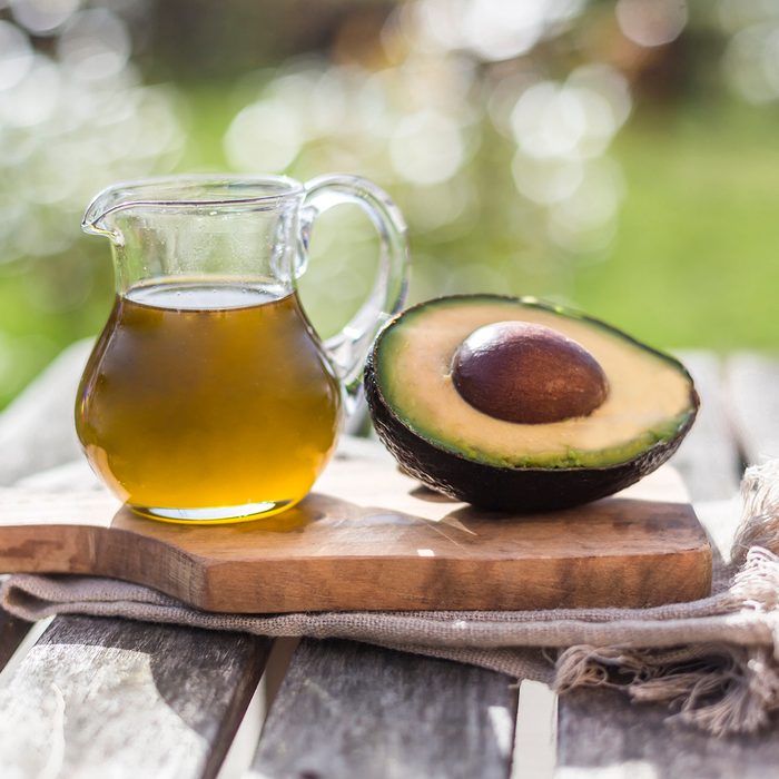 healthy oils Half of avocado and glass jug of avocado oil on wooden board