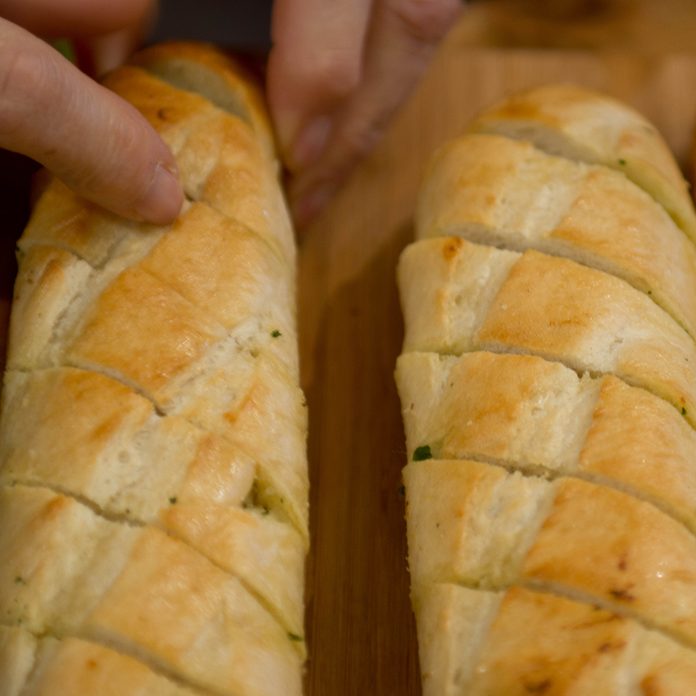 types of french bread Whole garlic baguettes on a bread board being pulled apart by someone's fingers.