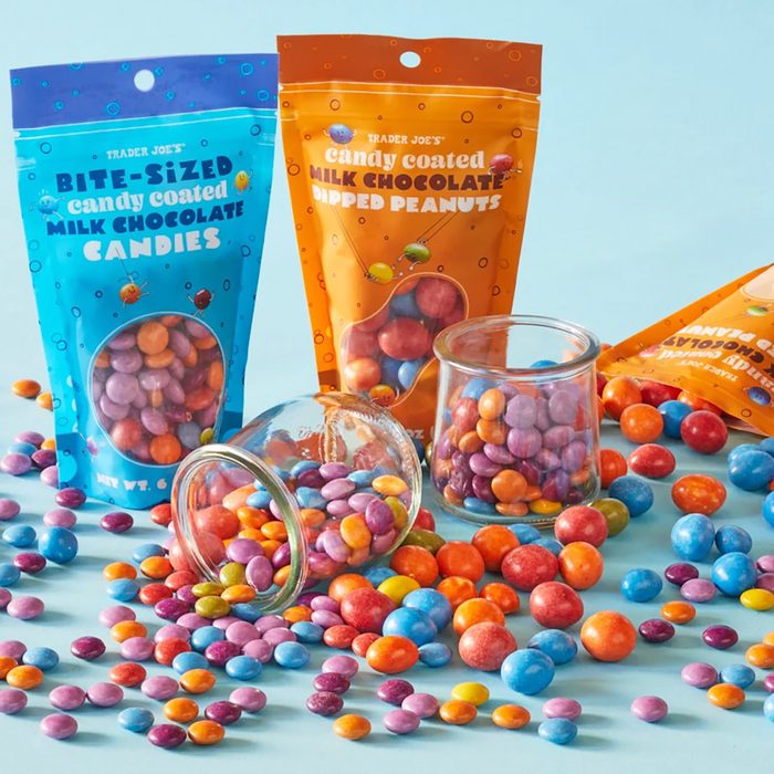 Colorful Trader Joe's Milk Chocolate Candies and Dipped Peantus in small glass jars, and sattered on blue surface