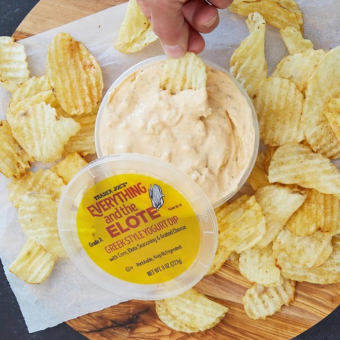 Trader Joe's Everything and the Elote Greek Style Yogurt Dip opened, with a chip being dipped, and surrounded by more chips