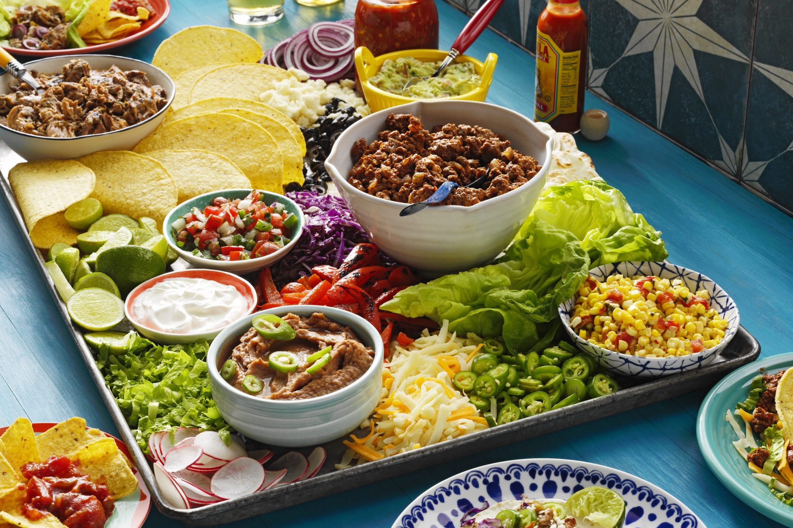 Taco board with guacamole, chips, and salsa on blue wood background