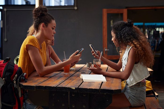 Young Women Looking At Their Own Different Phones And Tablet